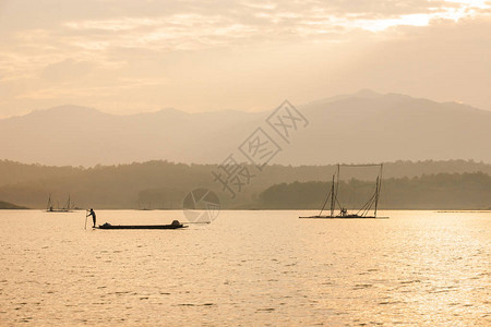 黄昏时分在湖边钓鱼的渔夫木筏底网和山峰图片