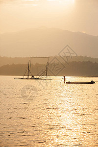 黄昏时分在湖边钓鱼的渔夫木筏底网和山峰图片