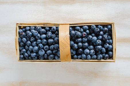 白木背景的篮子中新鲜有机蓝莓图片