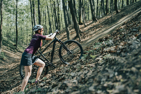 女运动员在夏日骑脚踏车到林中山丘头盔的图片