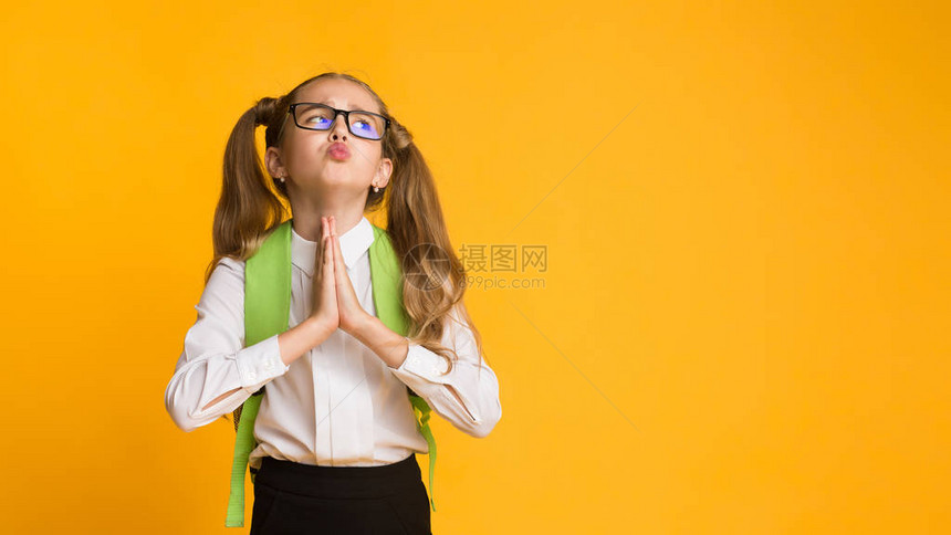 可爱的小学生女孩在工作室里要求用双手在黄色背景上祈祷的东西图片