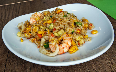 木桌上的碗盘里有混合海鲜和鸡蛋的米饭亚洲传统美食图片