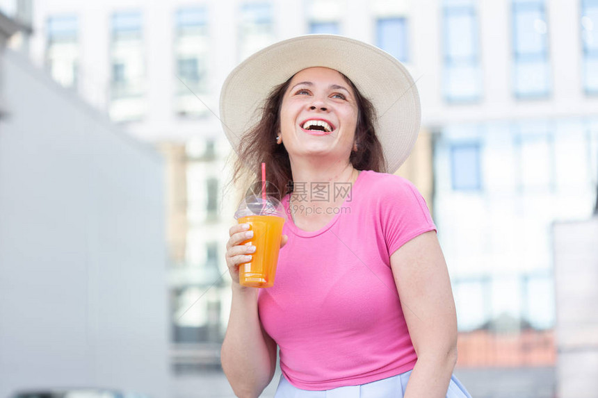 一个年轻美丽开朗的女人戴着帽子在温暖的夏日带着果汁在城里走来去的底部视图肖像周末漫图片