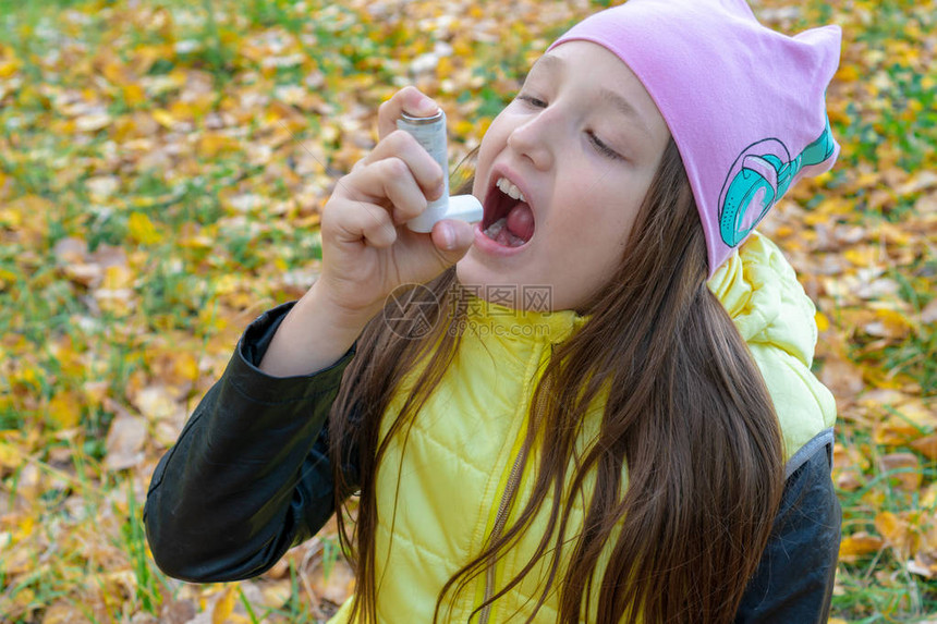 一个戴着帽子和夹克的女孩在秋天的森林里散步时以吸入器的形式服用治疗支气管哮喘的药物流感季节和感冒鼻炎过敏的孩子图片