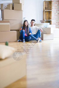 坐在新房地板上的亚洲年轻夫妇围着纸板箱放图片