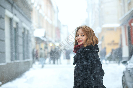 红嘴唇的月色黑发女孩在下雪时穿着大衣和围巾图片