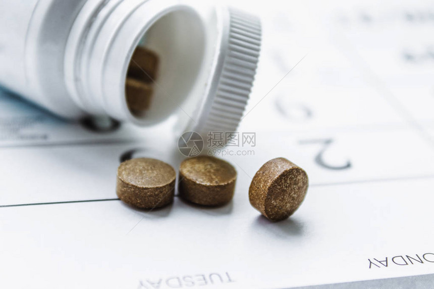 白罐子旁边的小黑药片或日历背景上的瓶子该病的治疗方图片