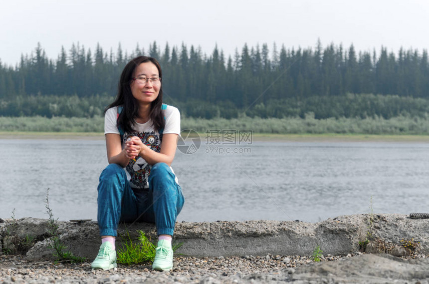 微笑的运动雅库特亚洲女孩戴着眼镜坐在北针叶林的Vilyui河的旧码头上图片