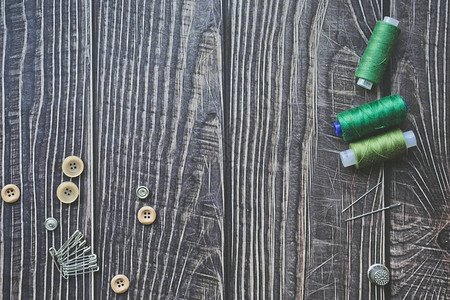 深色木制背景上的缝纫配件绿色缝纫线针按钮和别针顶视图图片