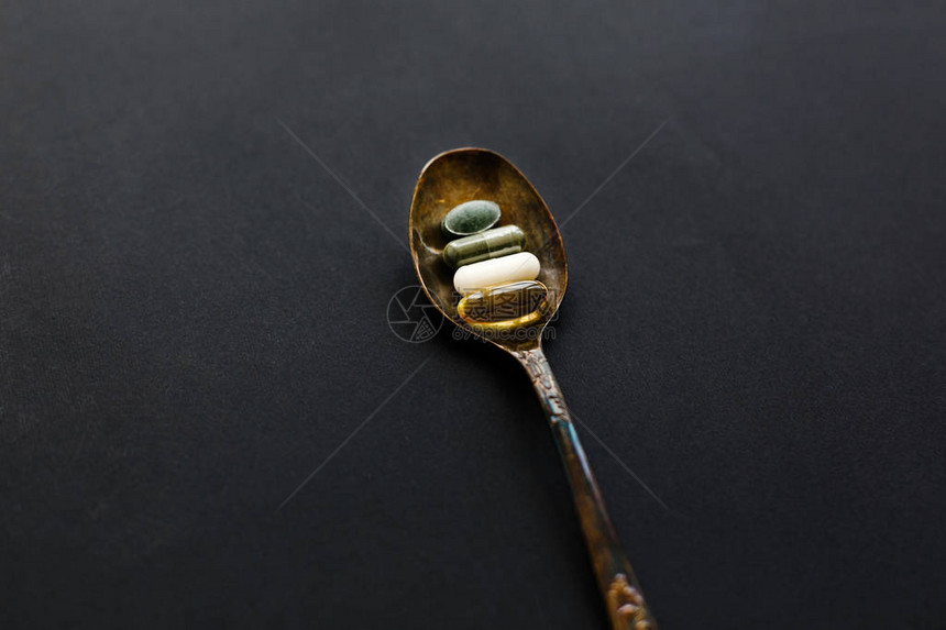 黑色深背景上勺子上的欧米茄3螺旋藻叶绿素镁胶囊膳食补充剂健康支持和治疗生物活添加剂每图片
