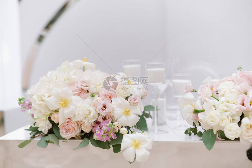 现代婚礼餐桌的时尚装饰与浅色调的白色蜡烛和鲜花白色蜡烛和各种新鲜美丽鲜花的束装图片