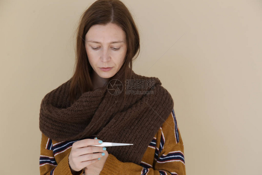 工作室拍摄的年轻发烧女人裹着羊毛围巾在温度计上图片