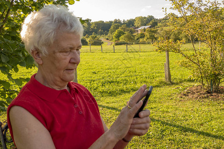 高龄公民在花园的手机上检查您的留言请访问InfoF图片