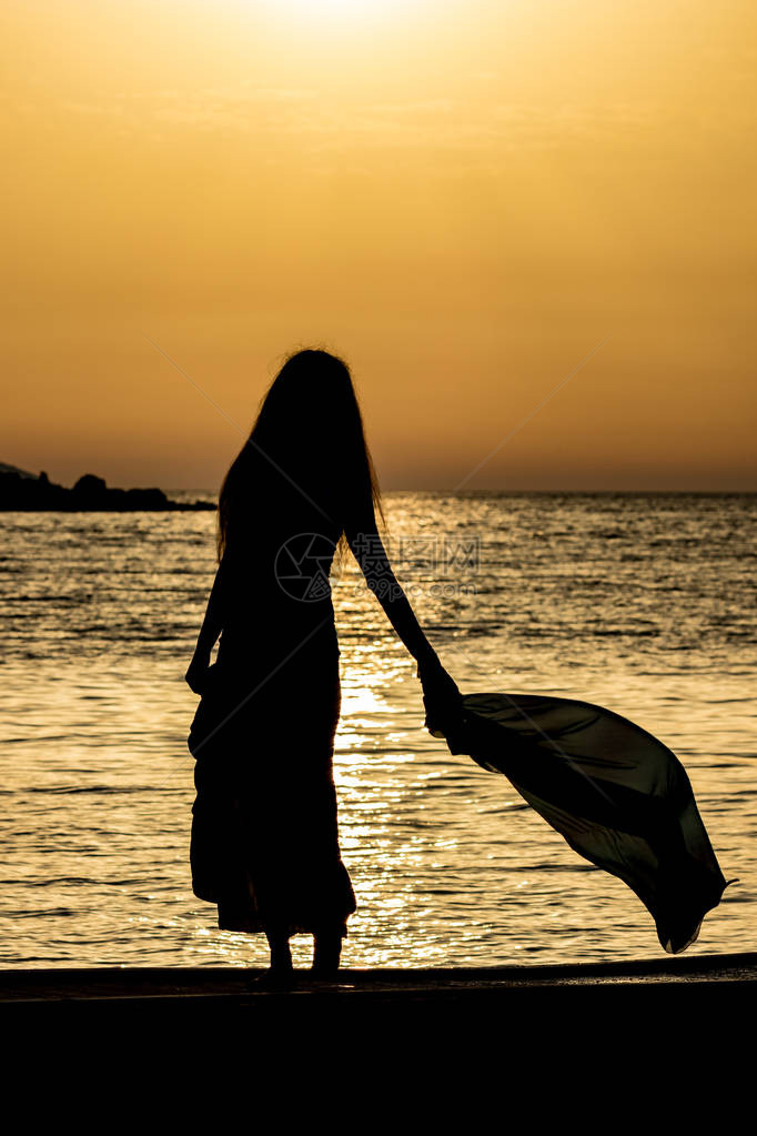 美丽的女剪影无法辨认的苗条高个女人与丝巾在金色的爱奥尼亚海水前夕阳从阿尔巴尼亚卡萨米尔看到的五颜六色图片