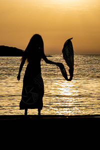 维巴尼亚美丽的女剪影无法辨认的苗条高个女人与丝巾在金色的爱奥尼亚海水前夕阳从阿尔巴尼亚卡萨米尔看到的五颜六色背景