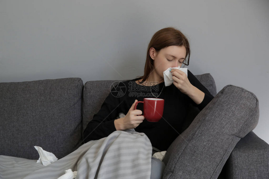 沙发上的年轻女人把鼻子吹进一张白纸巾有过敏症状的年轻女子在纸巾上打喷嚏的摄影棚流感图片