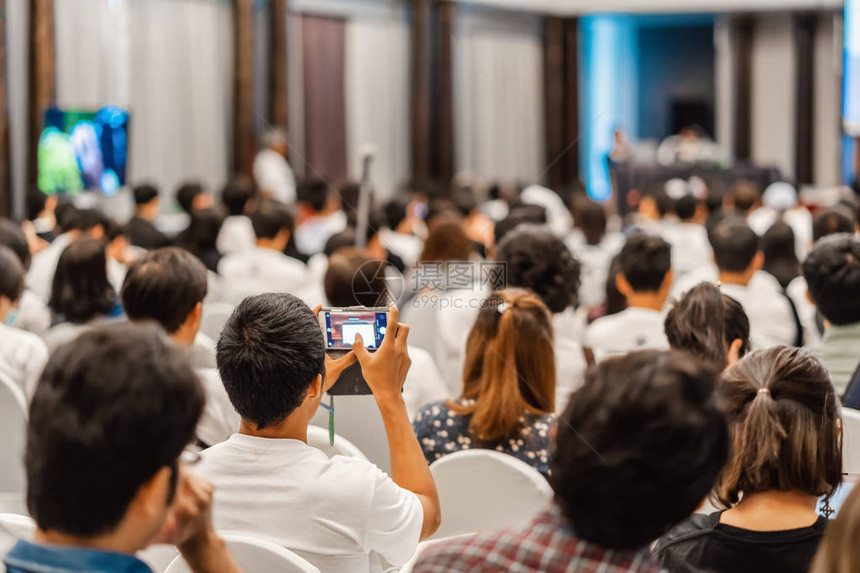 观众聆听演讲者的后视图和使用手机在会议厅或研讨会议和研讨会活动商业和投资概图片