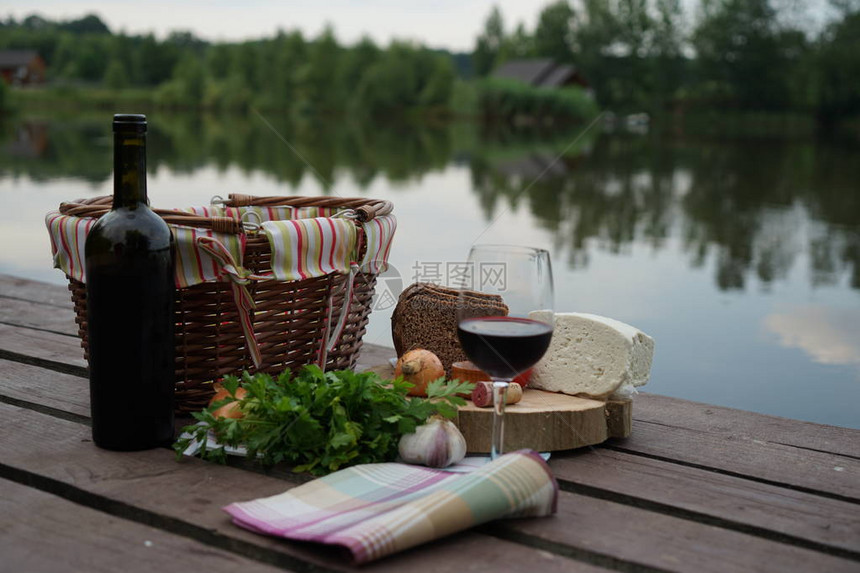 湖边码头上的一杯酒蔬菜和野餐篮图片