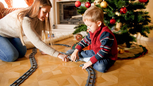 年轻母亲帮助儿子在客厅的圣诞树下修建玩具火车尾道图片