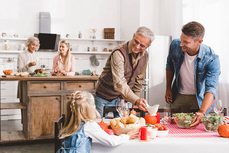 有选择焦点微笑的父亲和外祖父母看着孩子在感恩节放餐图片