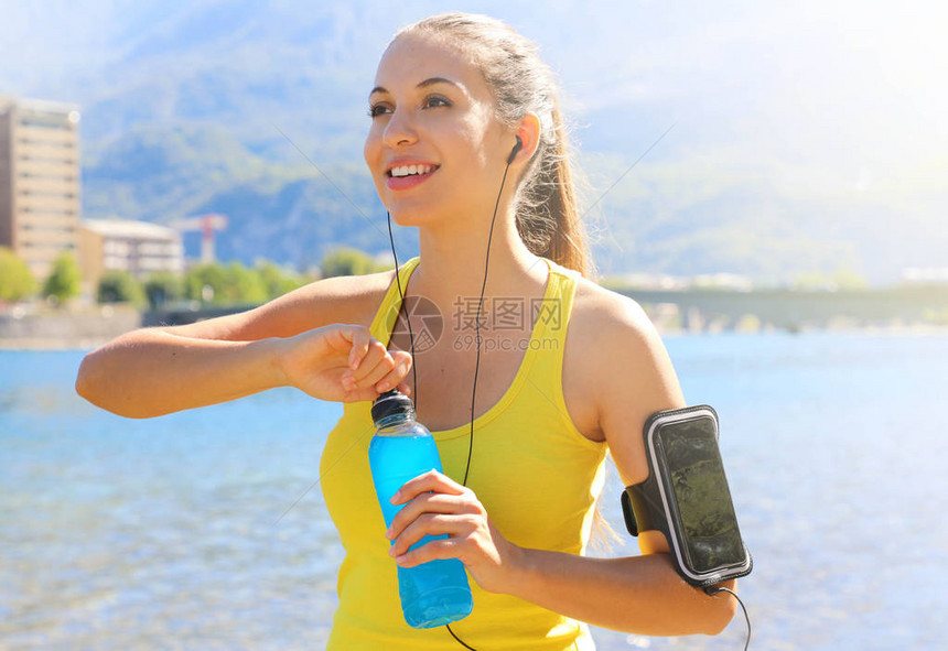拥有智能手机开源饮料瓶臂带的快乐女运动员在日常训练后图片