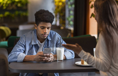 无聊的Afro男人在咖啡馆约会时看智能手机图片