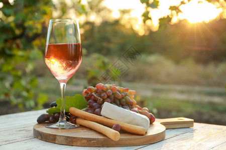 在葡萄园的木桌上放着一杯酒和小吃图片