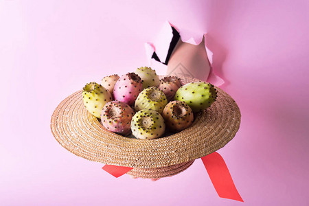手里拿着一顶时髦的粉红色背景上带刺梨果的草帽刺梨或FichiDindiaSalento图片