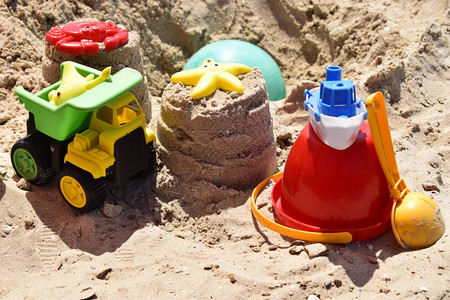 儿童塑料玩具绿尾黄车铁锹红桶黄沙绿球在海边沙滩上图片