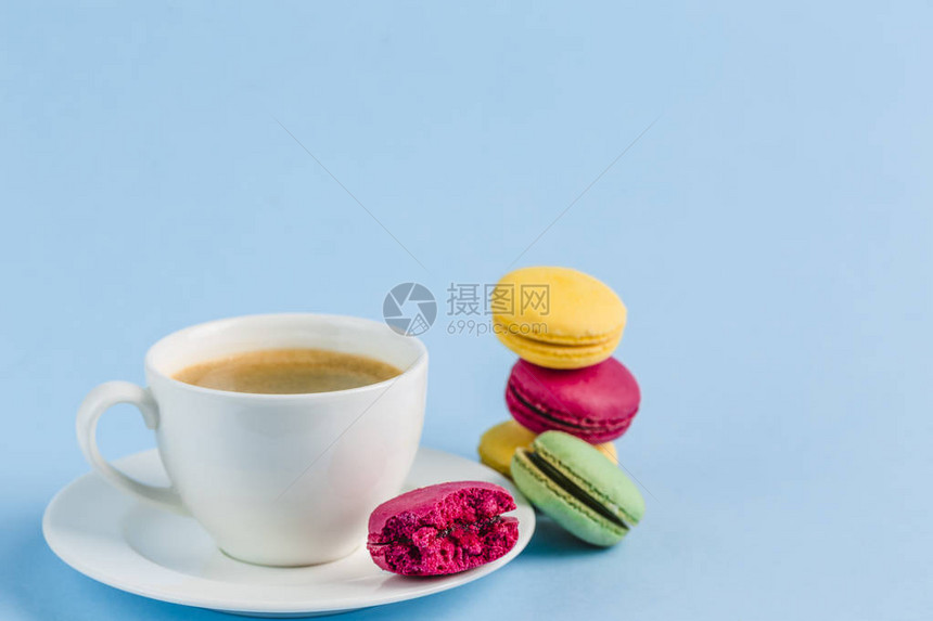 蓝色背景的白咖啡杯上多彩的马卡龙图片