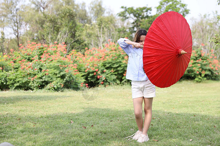 带着绿树和鲜花背景的红伞在公园中玩着红色雨伞的全弹图片