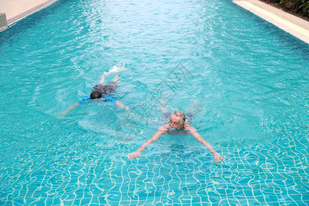高角度看快乐的白种老年丈夫和亚洲老年妻子在退休假期在游泳池游泳图片