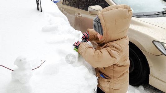 在寒冷的冬季清晨男孩用大刷子在雪落下图片