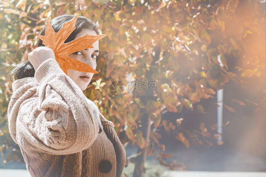秋季的概念一个美丽的中东女人拿着一片黄色的秋叶年轻女用秋天的树叶遮住她的脸秋天或秋天的女人在户外晴图片