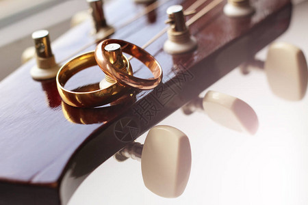 两个金结婚戒指躺在吉他琴弦上特写图片