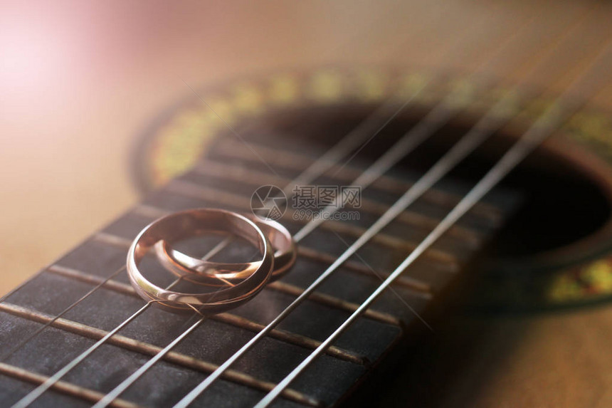 两个金结婚戒指躺在吉他琴弦上特写图片