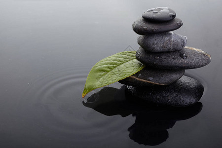 平衡桩中的禅石和带水滴的绿叶背景图片