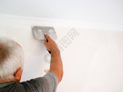 抹刀的男人白发男子在家修理墙壁对齐批发开商后视图男人用油灰刀抹灰墙图片