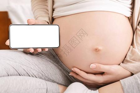 孕妇拿着手机靠近她的大肚子图片