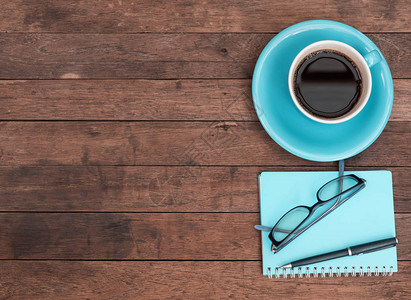 蓝色咖啡杯眼镜笔和记本在格朗基木桌顶背景上图片