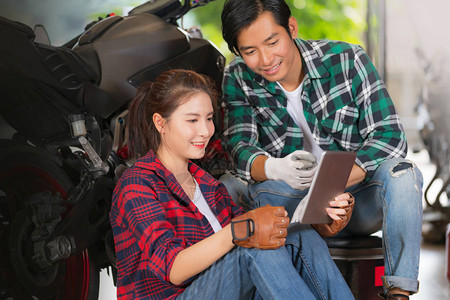 快乐的一对夫妇在修理和定制有摩托车背景的摩托车店使用数图片