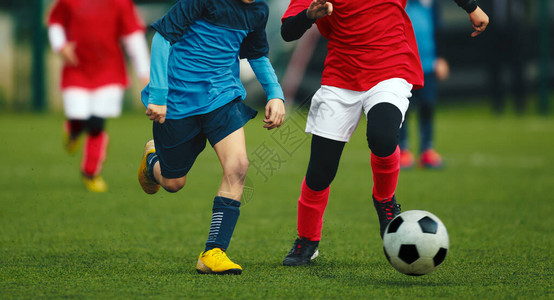 两名年轻足球员的决斗孩子们的足球比赛儿童训练和足球锦标赛初级足球比赛身穿红色和蓝色球衣的足球背景图片