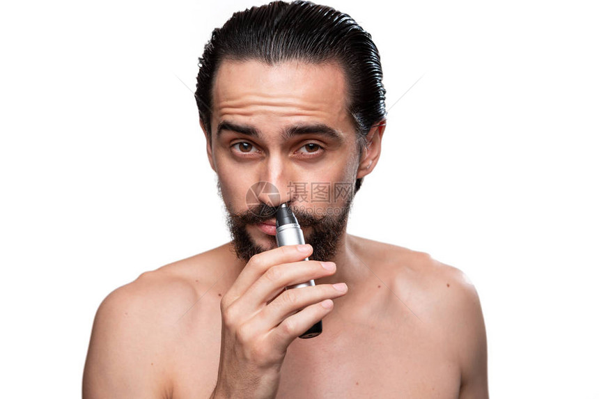 留着胡子的英俊大胡子男使用电动修剪器修剪鼻子上的头发图片