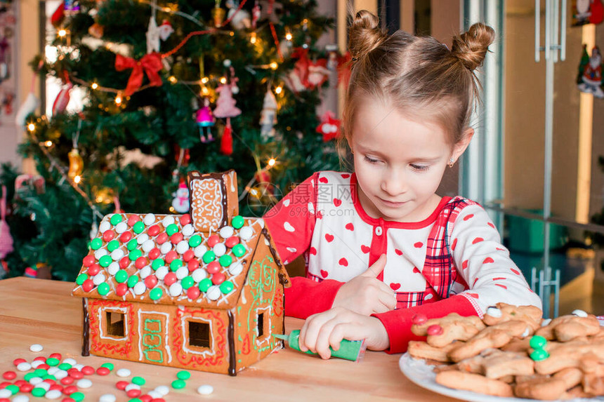 可爱的小女孩在姜饼房装饰着灯光和圣诞树的玻璃图片