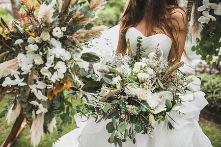 女人手握着博霍式的盛大的婚礼花束干燥的花朵白玫瑰和兰花图片