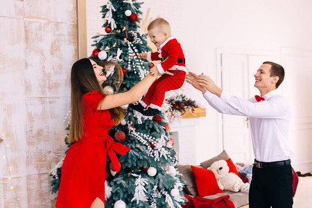 妈穿着红裙子抓住她儿子跟圣诞树旁边的孩图片