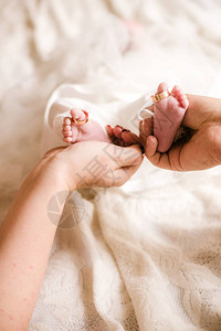 母亲和父亲的手在白床上抱着一个新生婴儿的小可爱腿在家中图片