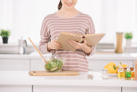 微笑的女人站在靠近碗的厨房桌子上阅读收据书的剪影图片