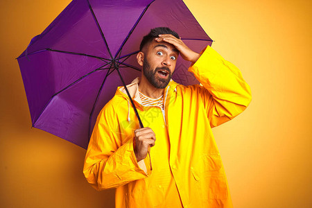 年轻的印度男子穿着雨衣和紫色雨伞图片