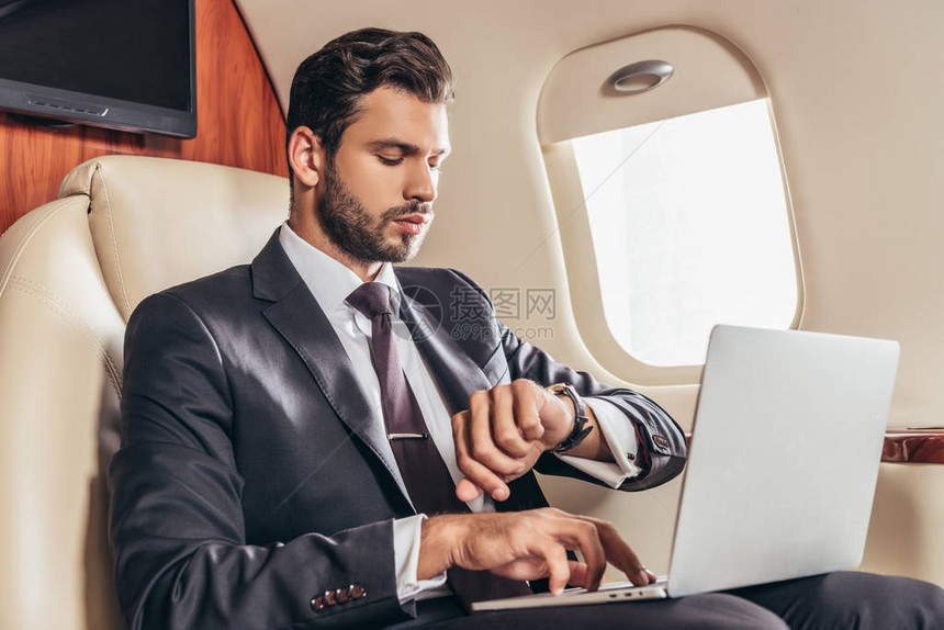 穿着西装使用笔记本电脑和在私人飞机上看手表的图片